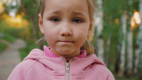 Portrait of sad little girl looking at camera. The face of seriously thinking, melancholy child, wailful kid in summer park outdoors, close up.