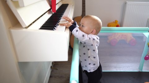 A cute baby boy trying to play a big piano while standing up. 4K