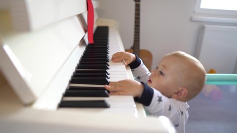 A cute baby boy trying to play a big piano while standing up. 4K