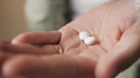 Two white pills fall on a woman palm from bottle of pills. Close-up