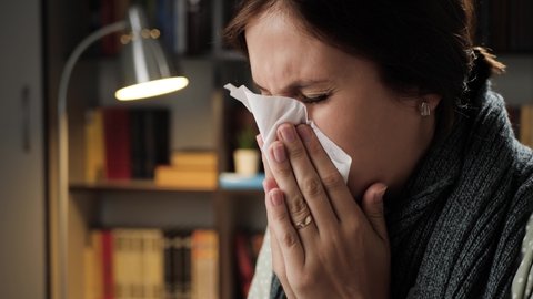 Cough, sneezing, runny nose. Woman at workplace in evening coughs and wipes her nose with napkin. Cold, flu, allergy, coronavirus, covid-19 concept. Close-up
