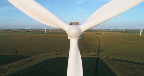 Aerial close up view of wind turbine rotor with blades rotating slowly on wind farm at sunset. Slow motion