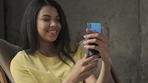 Young happy woman talking by videocall by mobile phone indoors at home