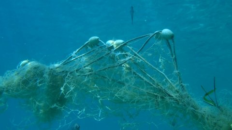 Lost fishing net with buoys lies underwater on the seabed. Problem of ghost gear - any fishing gear that has been abandoned, lost or otherwise discarded. It is the most harmful form of marine debris