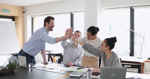 Motivated multicultural happy business people give high five at office meeting. African, caucasian and indian employees team celebrate leadership, professional success, good teamwork strategy concept.