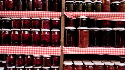 Glass jars with various types of natural delicious jam stand in a row on wooden shelves. Food background. Slow motion steadicam shot