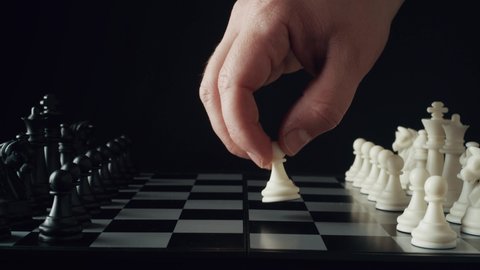 Game of chess. Male hand puts a white chess piece pawn on the chessboard on a black background. The concept of business strategy, startup, success. Depth of field. Red camera, 4K UHD