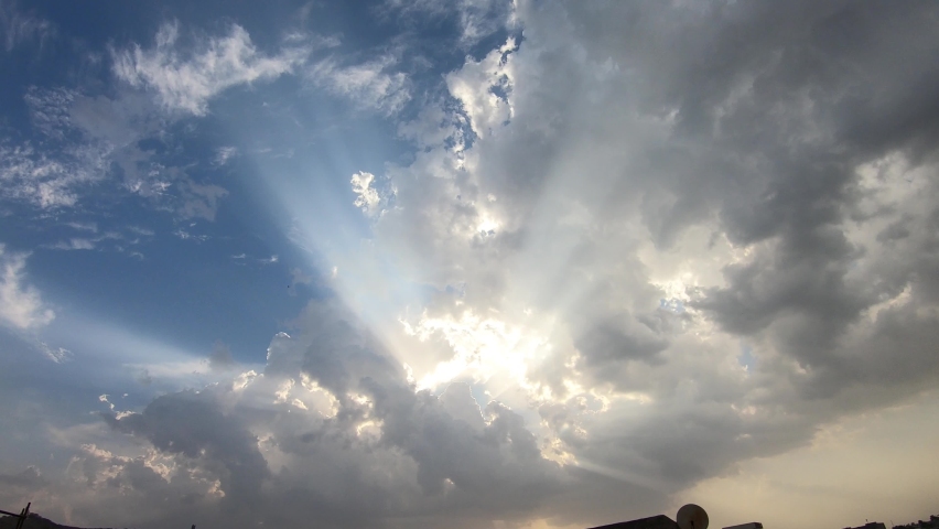 4K time lapse wide shot looking up at the sun shining and casting a lens flare in a blue sky as a fluffy white cloud approaches and obscures it sending light rays and shadows from the cloud	 | Shutterstock HD Video #1058621761