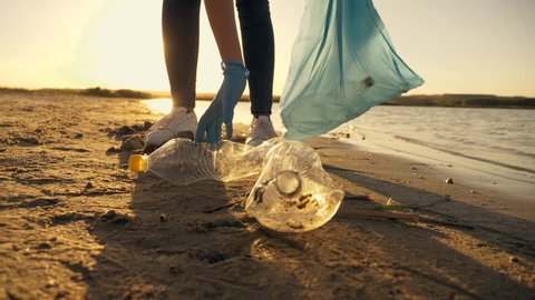 Teamwork cleaning plastic on the beach. Volunteers collect trash in a trash bag. Plastic pollution and environmental problem concept. Voluntary cleaning of nature from plastic. Greening the planet