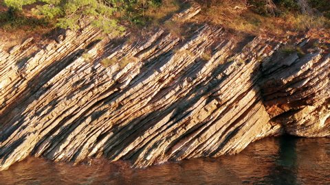 Layered rock formation on the shore. Dipping sedimentary rock strata. Texture of a sliced cliff by the sea, on the Adriatic coast of Montenegro.