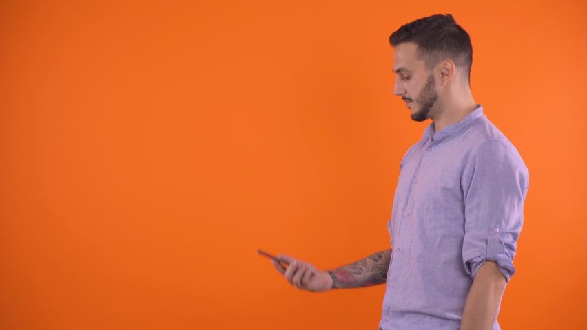 Man with tattoo sleeve on arm using smartphone to video call a friend, studio shot