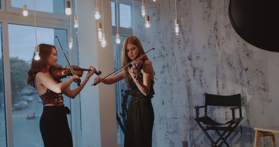 Beautiful duet of admiring women playing the violins at window indoor. Slowly in 4K