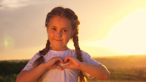 A little girl stands in the Park at sunset making a heart shape with her hands. Symbol of a healthy heart, love. Mother's day. World