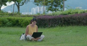 Woman work on laptop computer and sit on green lawn