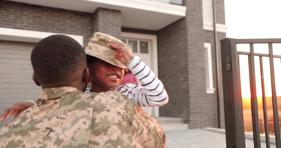 Happy African American woman wife with small kid meeting man husband after army outdoor at big house in outskirt. Male soldier coming back home to family and playing with cute daughter. Royalty-Free Stock Footage #1058626846