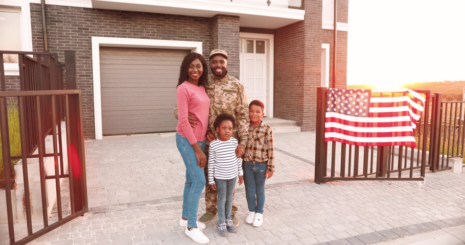 Portrait of African American family with little kids and father soldier. Outdoors in yard at home with USA flag. Husband and dad coming back home from war. Male officer with wife and small children. Royalty-Free Stock Footage #1058626858