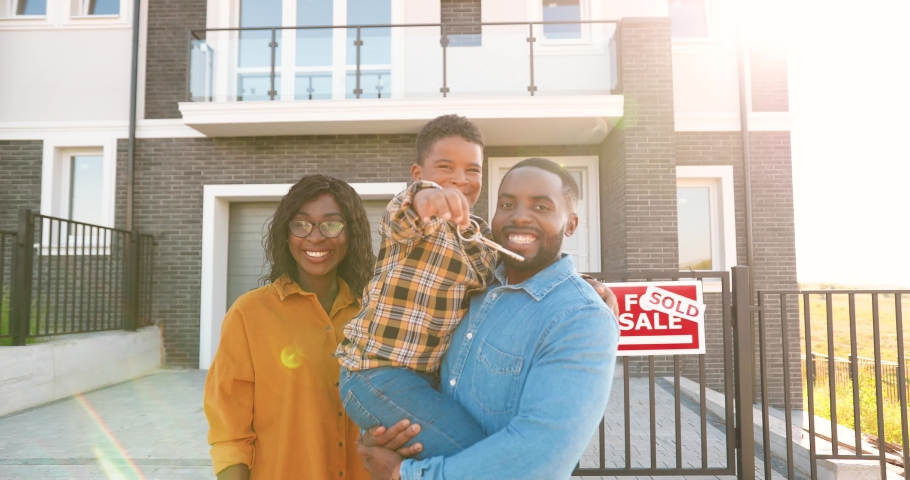 Portrait of happy African American family with small child standing at new house at suburb and demonstrating keys to camera. Cheerful parents and son showing key and moving in new home. Sold. Royalty-Free Stock Footage #1058626870