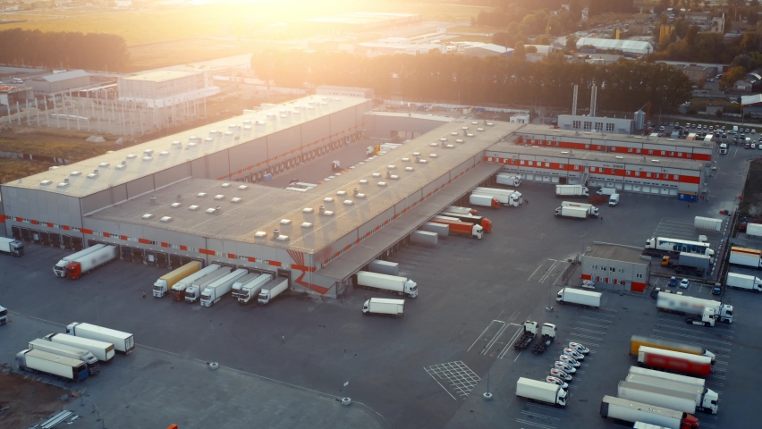 Logistics park with warehouse and loading hub. A lot of semi trucks with cargo trailers awaiting for loading/unloading goods at sunset. Aerial view  | Shutterstock HD Video #1058629867