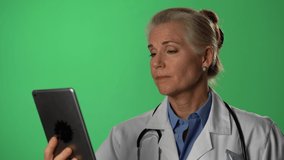Male doctor wearing a lab coat and stethoscope giving medical advice directly to phone in a hospital or medical office consulting with a patient via a video conferencing call on green screen.
