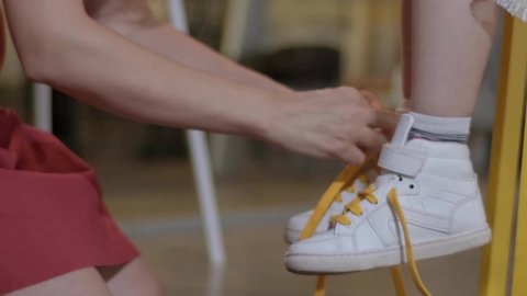 Mother ties her daughter's shoes.Mother ties laces of her daughter's sneakers. The mother's hands tie shoelaces to the legs of the child wearing shoes. Childcare and motherhood concept.