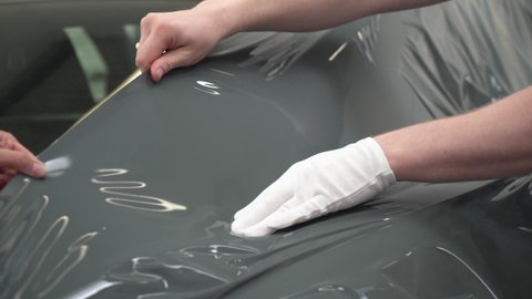 Close up shot of application of vinyl wrap film to sports car. Workers installing car wrap film by hand.