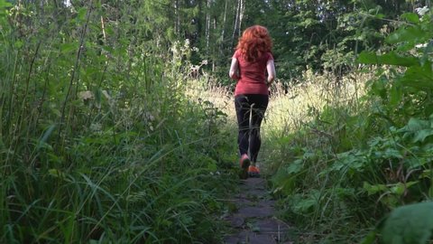 Slender and athletic middle-aged red-haired woman is engaged in running outdoors ,slow motion