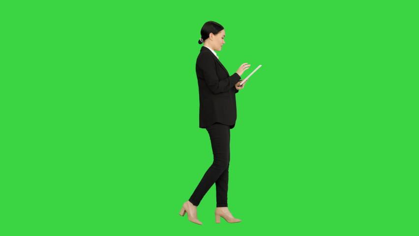 Smiling Businesswoman using computer pad while walking towards the camera on a Green Screen, Chroma Key.