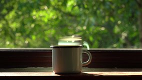 Empty metal blue mug standing on windowsill of window of rural cottage in countryside.