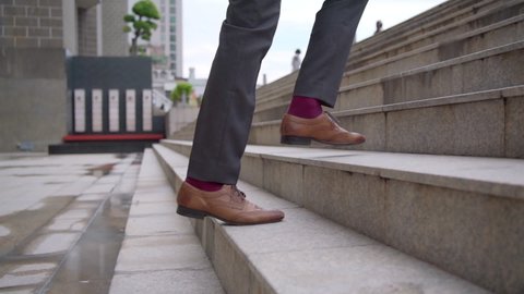 Slow motion legs of Business man office worker in suit and leather shoe walking up the stairs in rush hour at office district to work. Businessman entrepreneur ascend a staircase in the city.