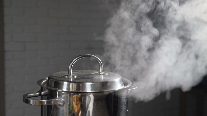 Steam or Vapour clouds rising from boiling water in saucepan on stove. Steam from pan while cooking. Cooking process in slow motion. Steam and white smoke rising on dark background. Full hd Royalty-Free Stock Footage #1058638984