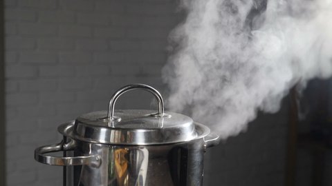Steam or Vapour clouds rising from boiling water in saucepan on stove. Steam from pan while cooking. Cooking process in slow motion. Steam and white smoke rising on dark background. Full hd