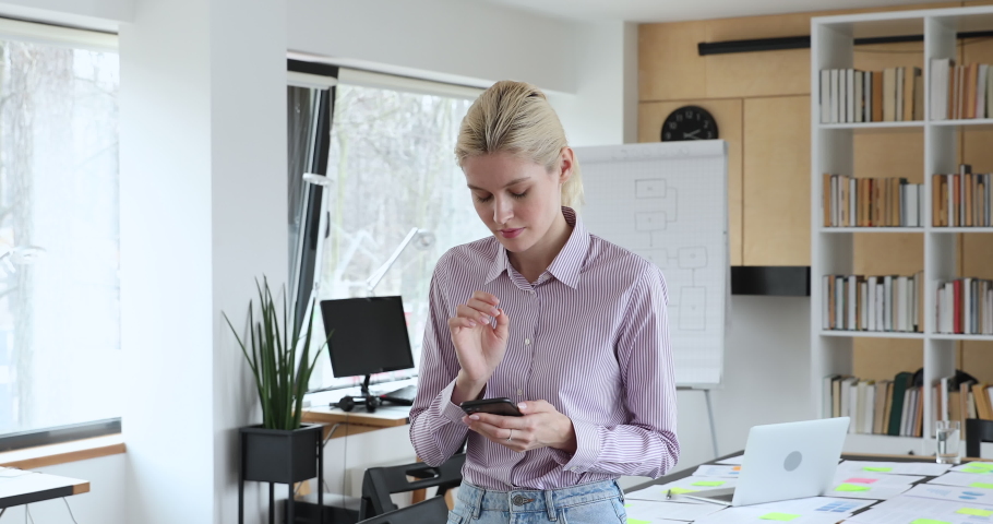 Blond focused female employee stand at office workplace hold cellphone typing message email to client consider about answer looking thoughtful. Chat distantly for business issue solution by smartphone Royalty-Free Stock Footage #1058642143