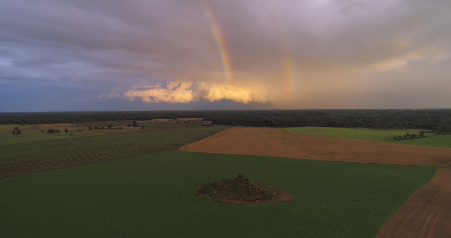 Aerial view of rainbow and clouds over agricultural field farmland at sunset