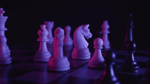 Chess pieces on a chessboard in a colorful fashion style. Studio neon light footage. Pink and purple colors. Slow tracking shot. Fashion, business concept. Depth of field, soft focus . Red camera