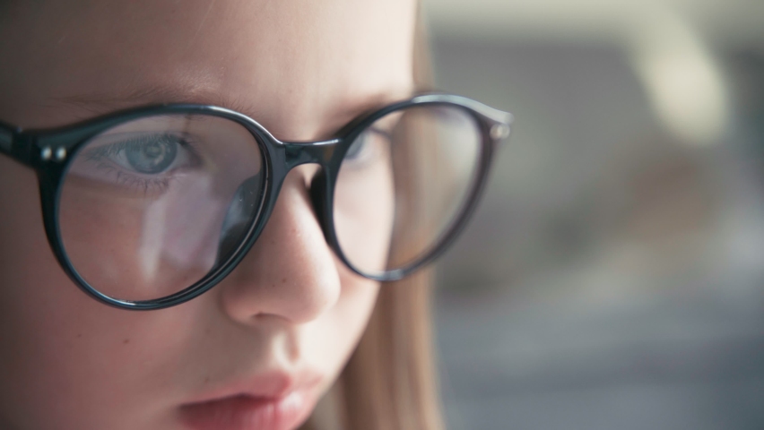 A close-up shot of a serious little 8 years old girl in glasses looking to a laptop screen. Remote education technologies and homework. Royalty-Free Stock Footage #1058649430