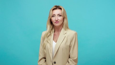 Bossy strict adult blond woman in business style jacket blaming and asking to get out, scolding with boyfriend, conflict, break-up. Indoor studio shot isolated on blue background