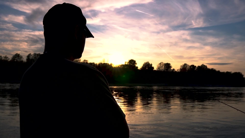 Angler is watching sunset on a river