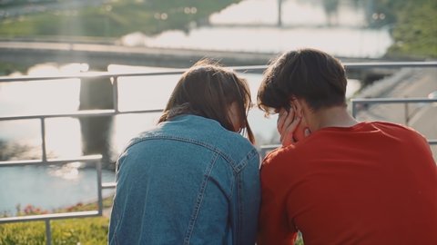 Young guy and girl sit on a bench with their backs to the camera and communicate. : vidéo de stock