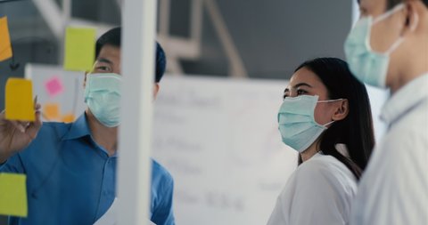 Portrait group of asian in medical mask in a diverse team of creative millennial coworkers in a startup brainstorming strategies. Three businesspeople coworking during meeting in office. : vidéo de stock