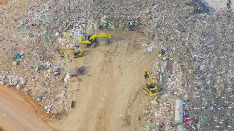 Aerial view of stack of different types of large mountain garbage pile, plastic bags, and trash with a tractor car in industrial factory in environmental pollution. Waste disposal in dumping site.