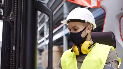 Portrait of a young man forklift driver with gloves and face mask in warehouse.