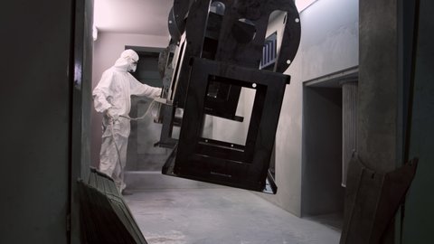 Male Worker In Full Protective Suit And Face Mask Holding Spray Paint Nozzle. Man paints large parts from production equipment. Professional metal painting. 4K FOOTAGE