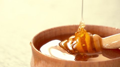 Liquid Organic Honey on a Special Honey Spoon in Wooden Bowl Close Up Shot. Healthy Food Concept. Honey Dripping to a Honey Dipper