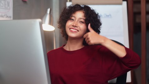 Happy Confident Asian Businesswoman looking at camera showing thumbs up hand sign gesture in office workplace. Female Freelancer Gesturing Like, Agreement and Job Done Sign by using a finger sign.