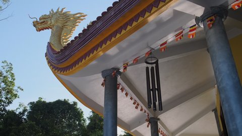 Low angle shot of Buddhist temple decorated with golden dragon. Hanging prayer flags and wind chimes. Ho Quoc Pagoda in Vietnam