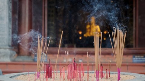 Slow motion of smoldering incense sticks with blurred Buddha statue in temple in background. Buddhism religion