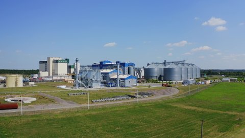 Agricultural industry. Modern factory on green field with steel elevators. Industrial buildings and granary under blue sky. Aerial view.