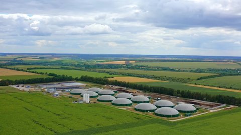 Biogas farm on green fields. Renewable energy from biomass. Modern agricultural biogas plant among beautiful environment. Aerial view.