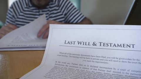 Man on the background reading and reviewing the details of a Last Will and testament document.