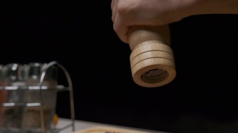 Close-up of a chef's hands grinding pepper with a hand pepper mill. Slow motion